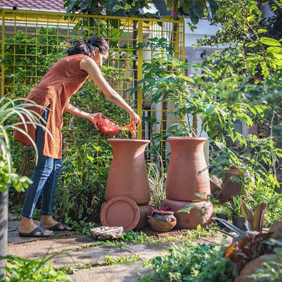 Pair of Daily Dump Prithvi Khambas home composters in outdoor garden with young girl adding kitchen waste to one.